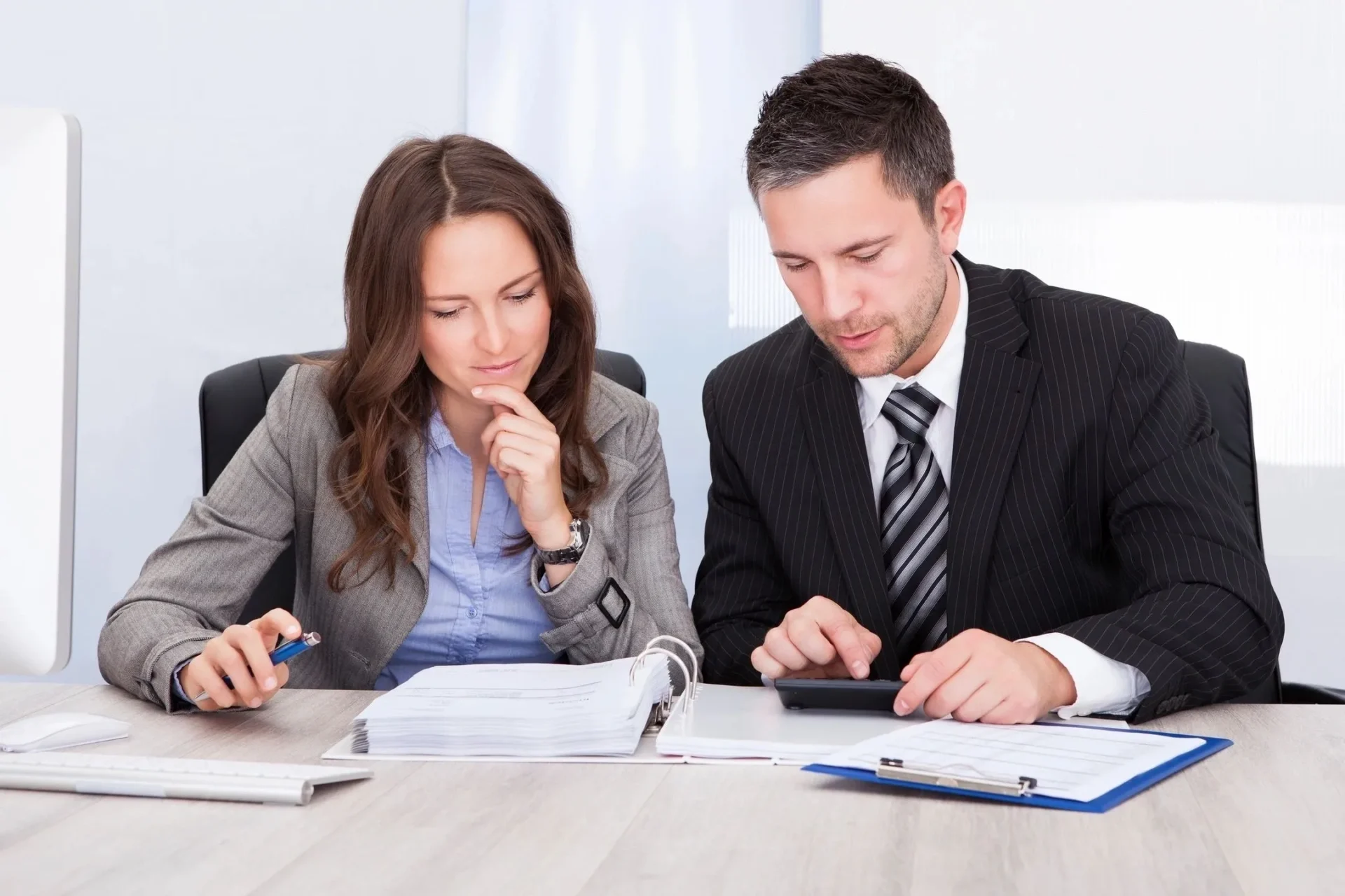 Two people sitting at a table with papers and calculators.